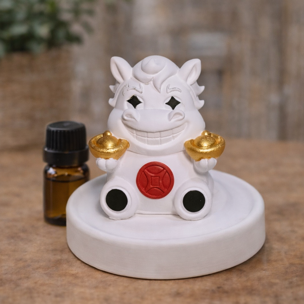 White figurine with black eyes and gold accents on a wooden surface next to a small bottle.