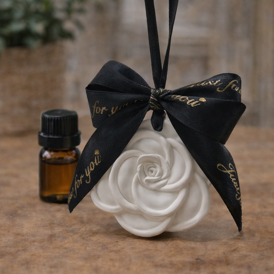 Decorative white rose with a black ribbon and bottle of essential oil on a wooden surface