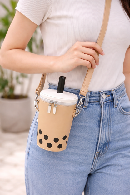Person holding a beige cup with black polka dots and a white lid, attached to a strap over their shoulder.